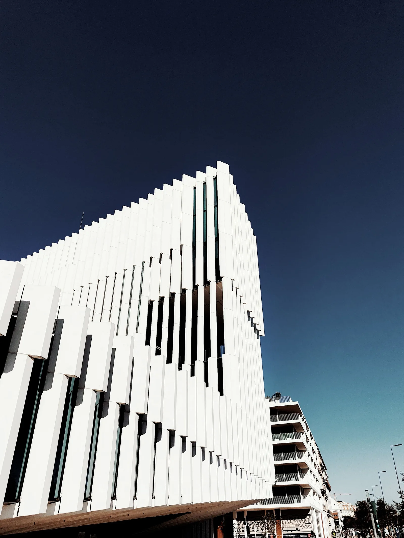 A white building wrapped in thin vertical fins against a deep blue sky