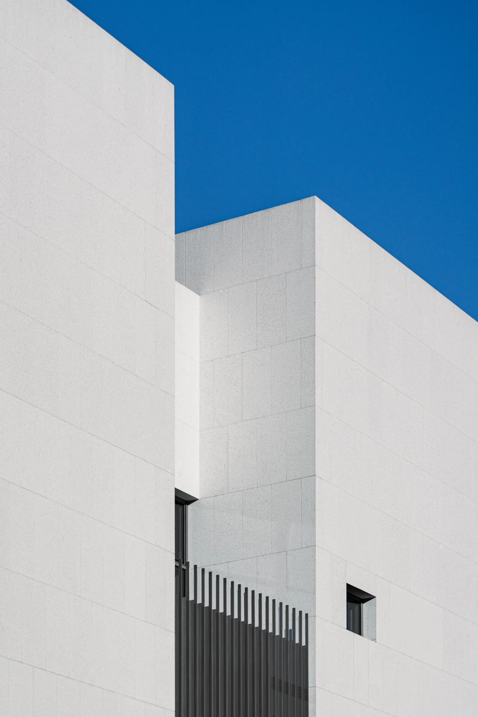 A white building with deep cut openings against a blue sky